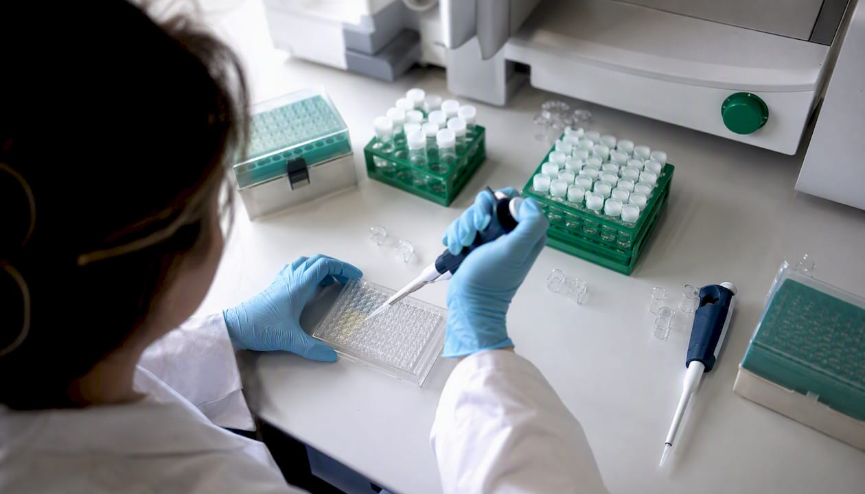 Gloved hands pipetting peptide sample into assay well plate